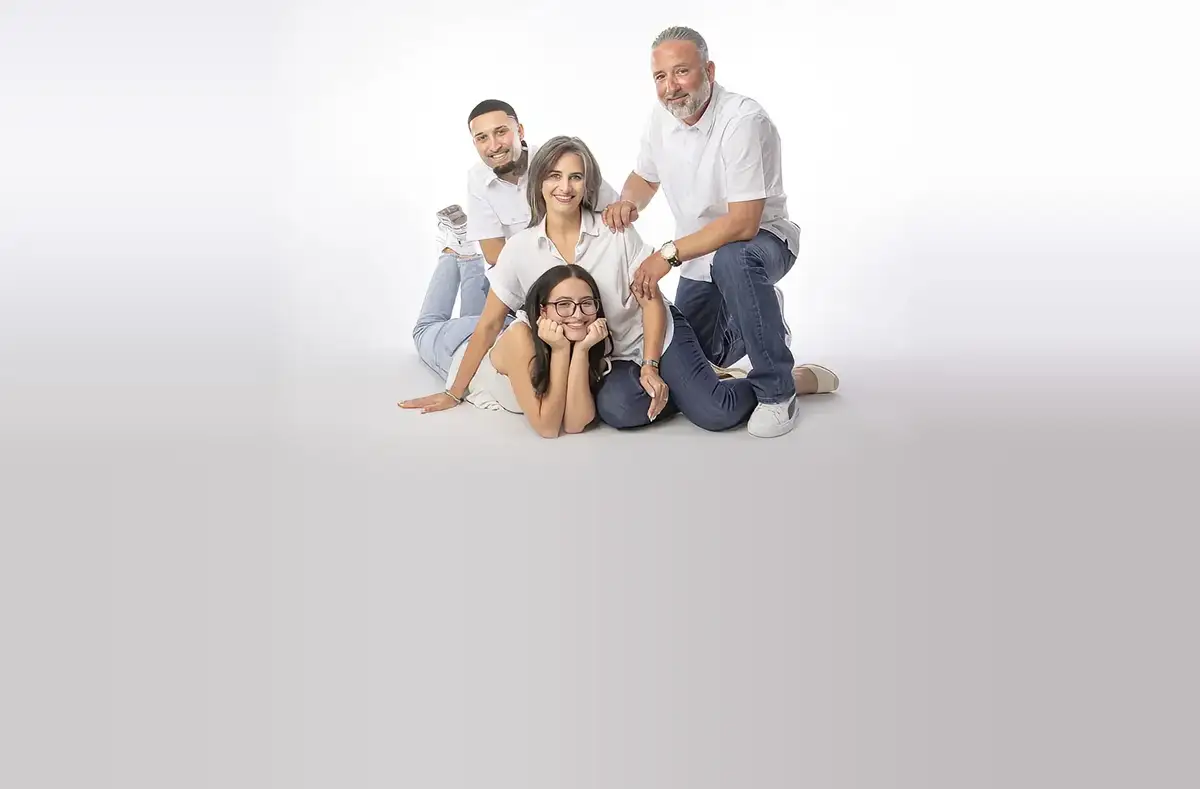 A family of four in white shirts and denim poses together, smiling, on a white studio floor